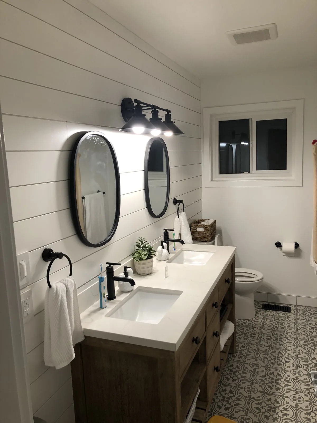 Renovated bathroom with a double vanity, round mirrors and patterned tile flooring