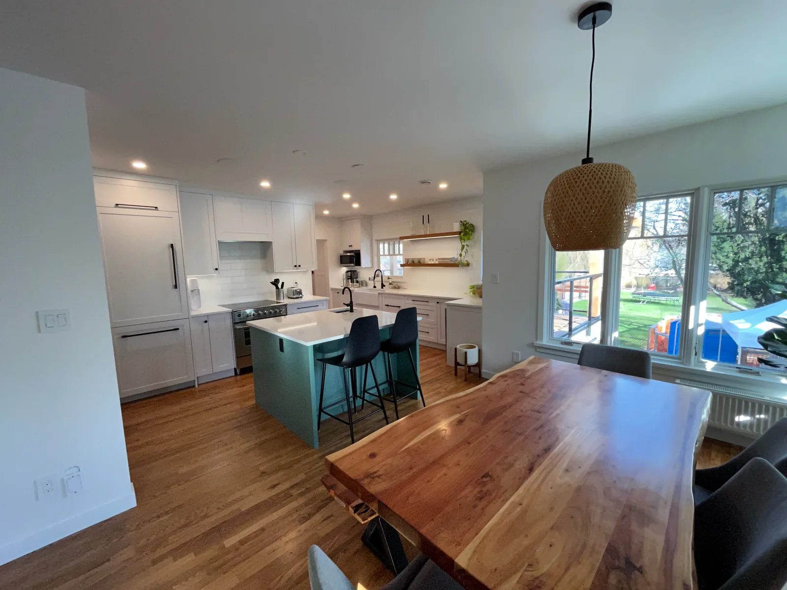 Open plan kitchen and dining area with a live edge wood table, hardwood floors and new windows, renovated by DM Patterson Construction in Victoria BC