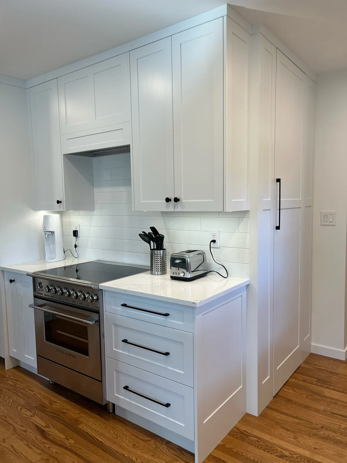 Renovated kitchen with white shaker cabinets, a stainless range, subway tile backsplash and hardwood flooring