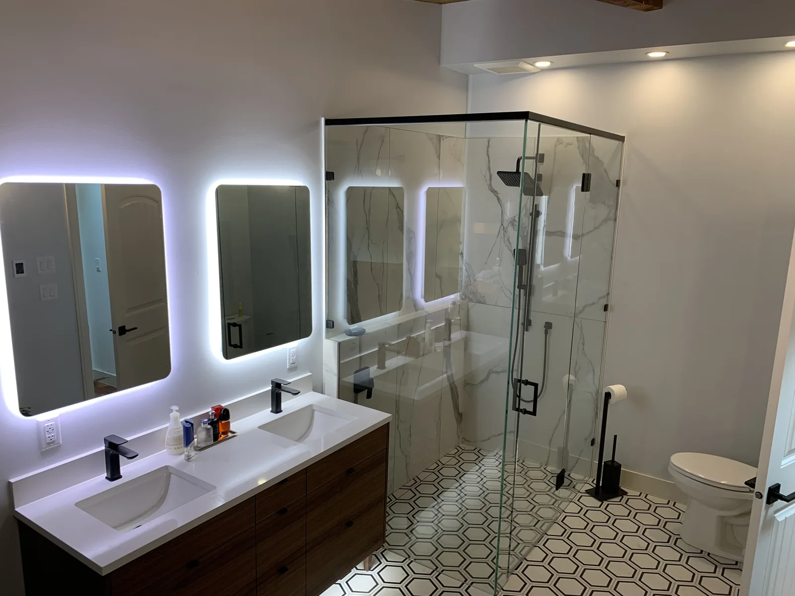 Renovated bathroom with a glass shower, double vanity and backlit mirrors